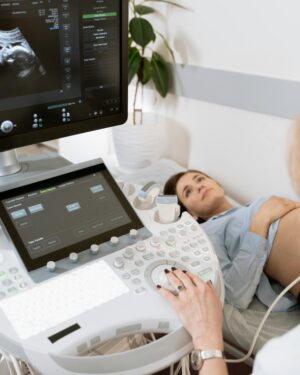 Pregnant woman undergoes ultrasound scan by medical professional in hospital room.